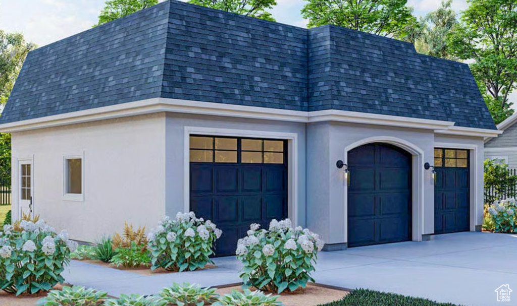View of front of home with a shingled roof, mansard roof, stucco siding, and concrete driveway
