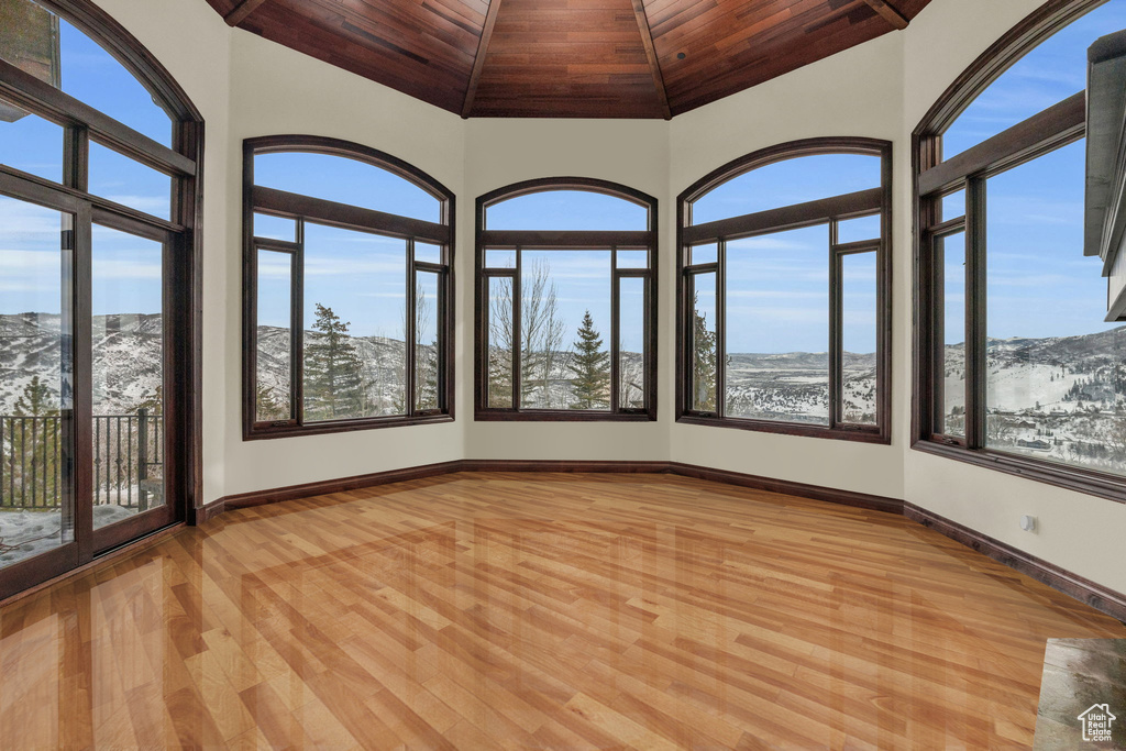 Unfurnished sunroom featuring wooden ceiling, healthy amount of natural light, wood finished floors, vaulted ceiling, and a mountain view