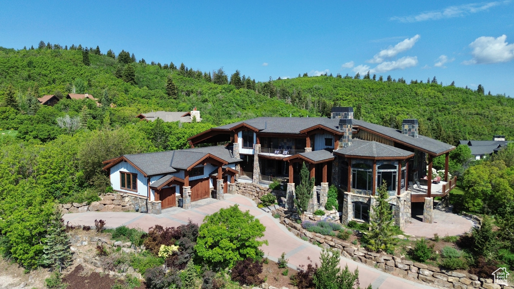 Rear view of house with a forest view, stone siding, a balcony, and driveway