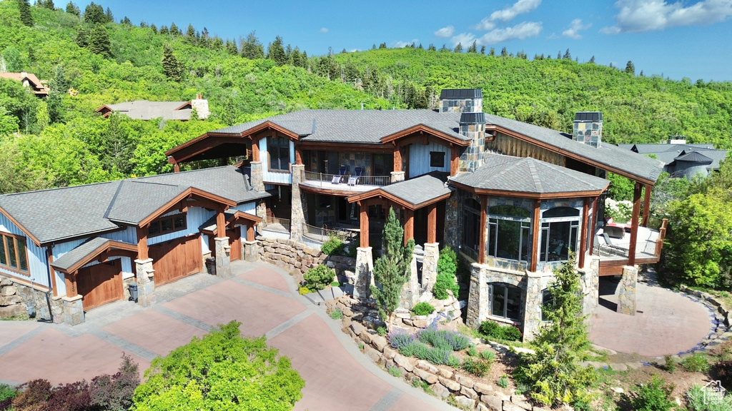 View of front facade with stone siding, a wooded view, a balcony, and driveway