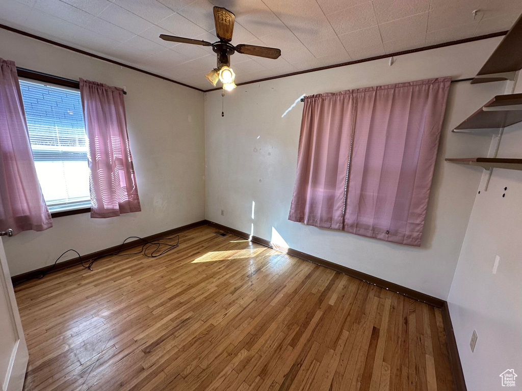 Empty room with crown molding, ceiling fan, and wood-type flooring