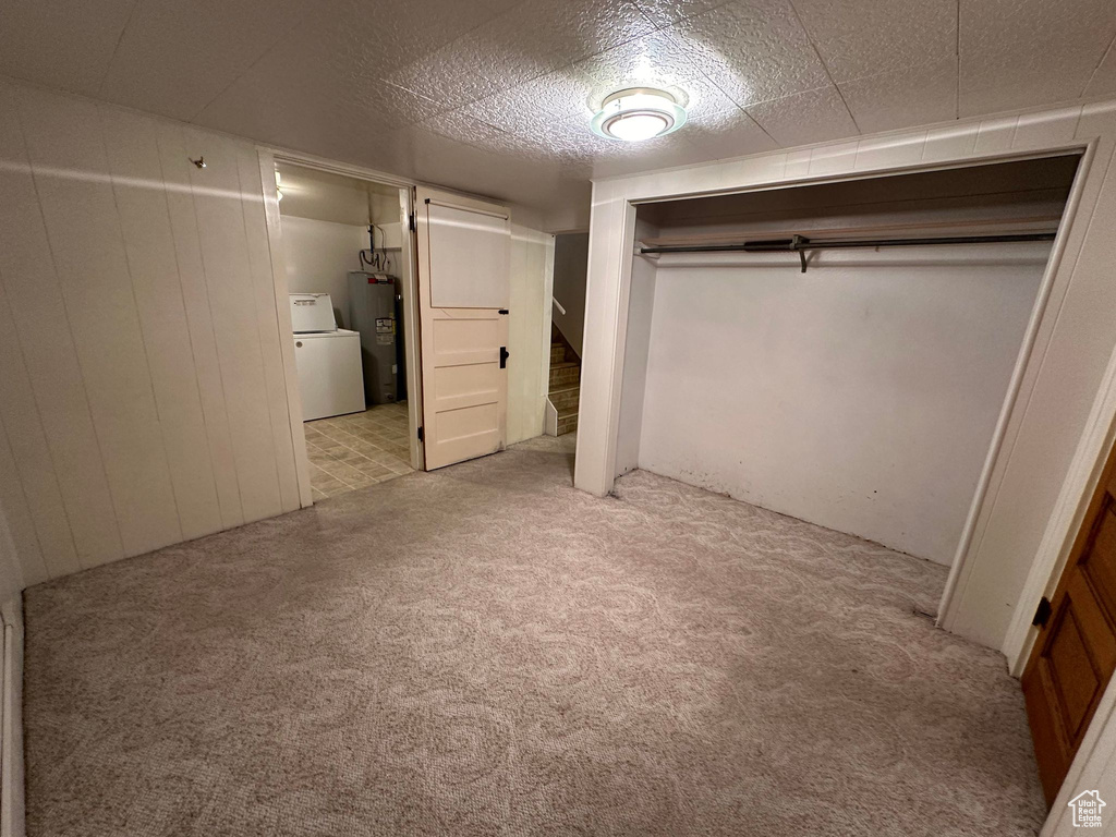 Unfurnished bedroom featuring light carpet, washer / dryer, wooden walls, and water heater