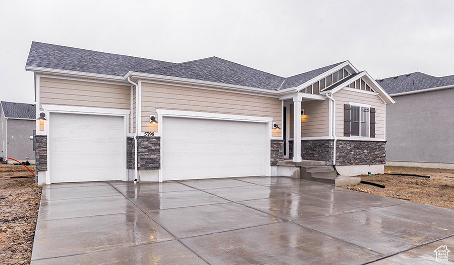 View of front facade featuring stone siding, an attached garage, driveway, and board and batten siding
