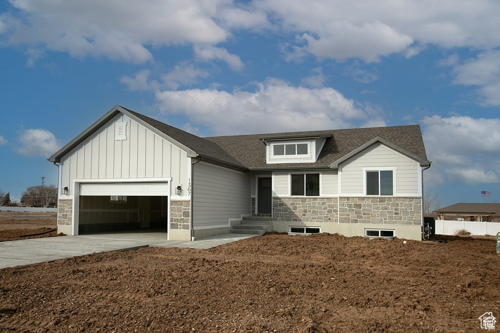 View of front of house featuring an attached garage, board and batten siding, driveway, stone siding, and roof with shingles