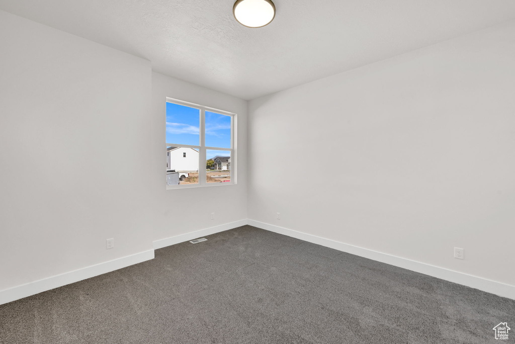 Empty room featuring baseboards and dark colored carpet