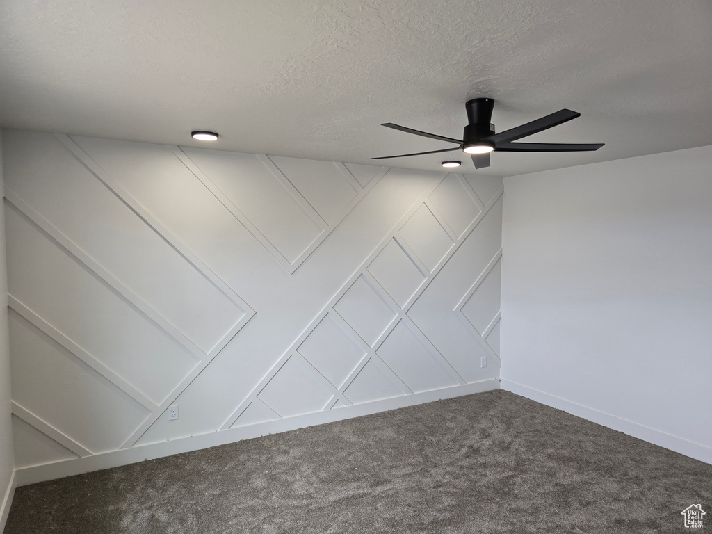 Empty room with carpet flooring, a ceiling fan, a textured ceiling, baseboards, and a decorative wall