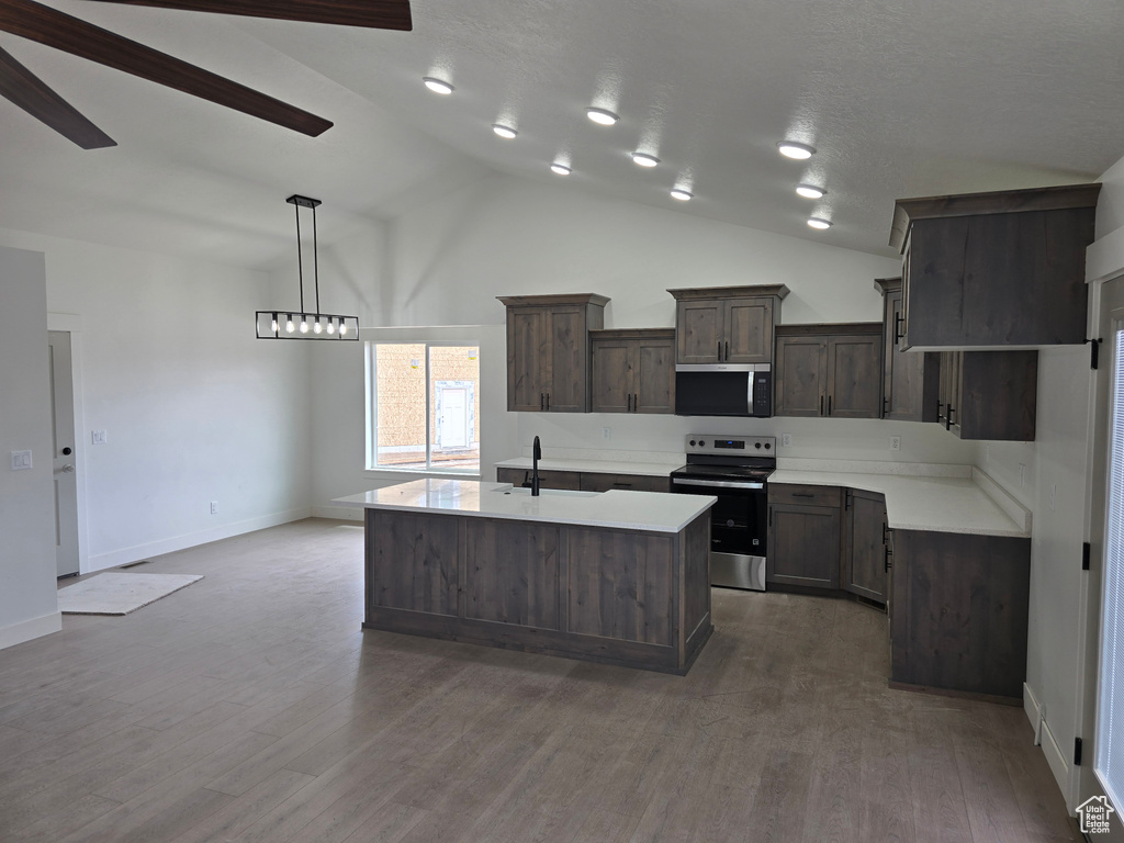 Kitchen with appliances with stainless steel finishes, light countertops, lofted ceiling, dark brown cabinets, and a kitchen island with sink