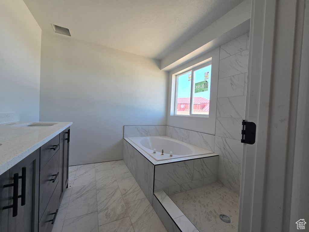 Bathroom with marble finish floors, vanity, and a bath