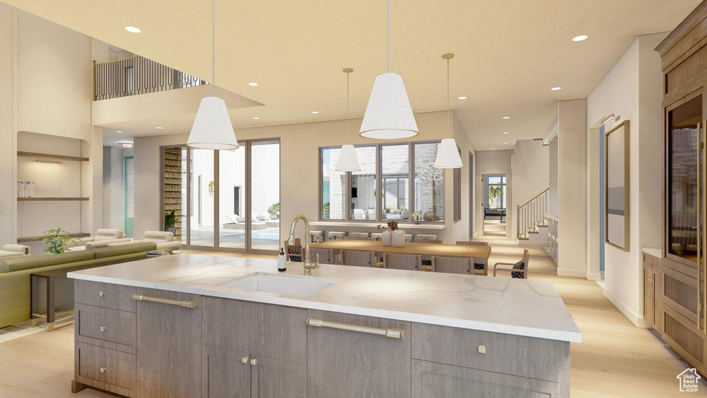 Kitchen featuring decorative light fixtures, sink, a large island, light stone counters, and light hardwood / wood-style flooring