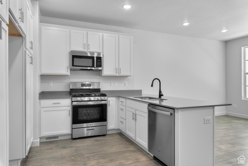 Kitchen featuring appliances with stainless steel finishes, sink, white cabinets, and kitchen peninsula
