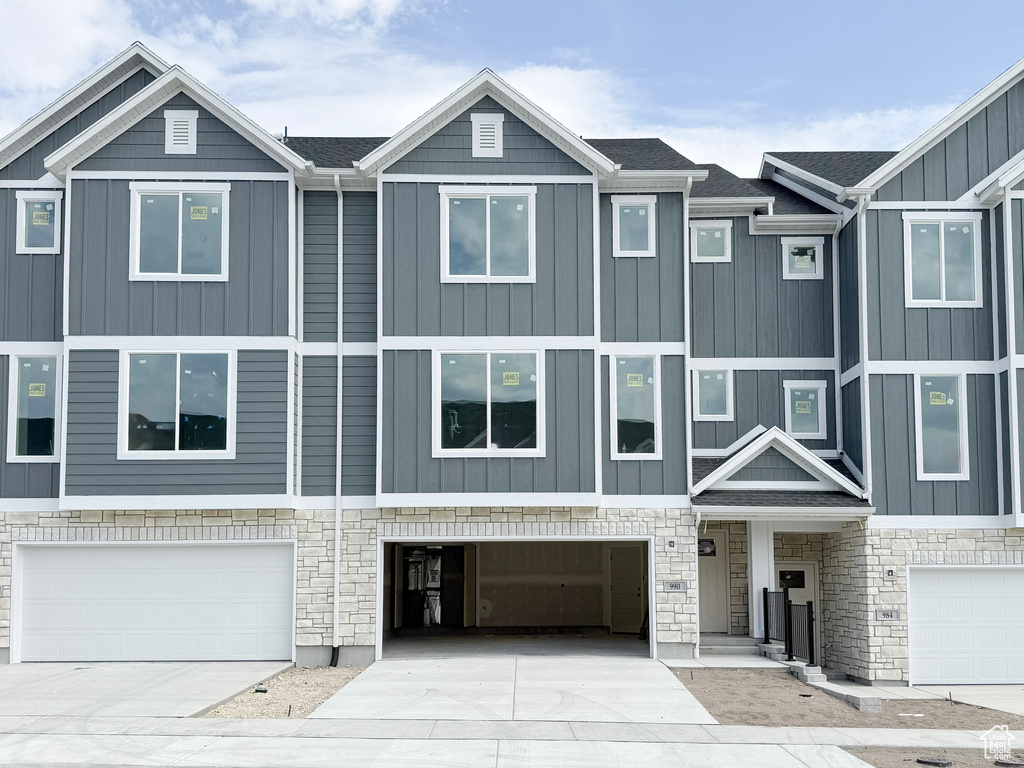Multi unit property featuring an attached garage, stone siding, and driveway