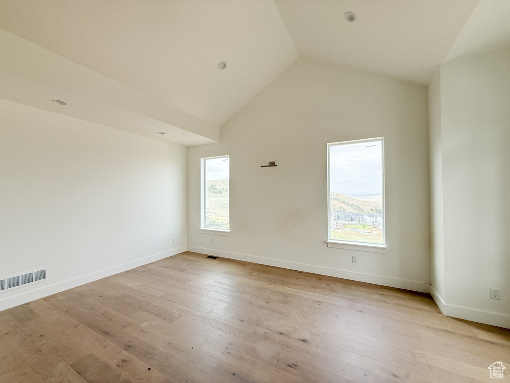 Spare room with plenty of natural light, light wood finished floors, and high vaulted ceiling
