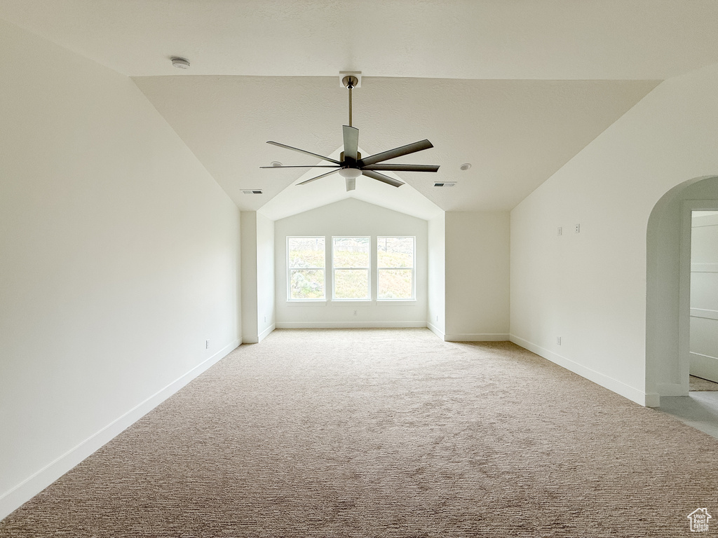 Unfurnished room featuring a ceiling fan, arched walkways, a smoke detector, lofted ceiling, and light colored carpet