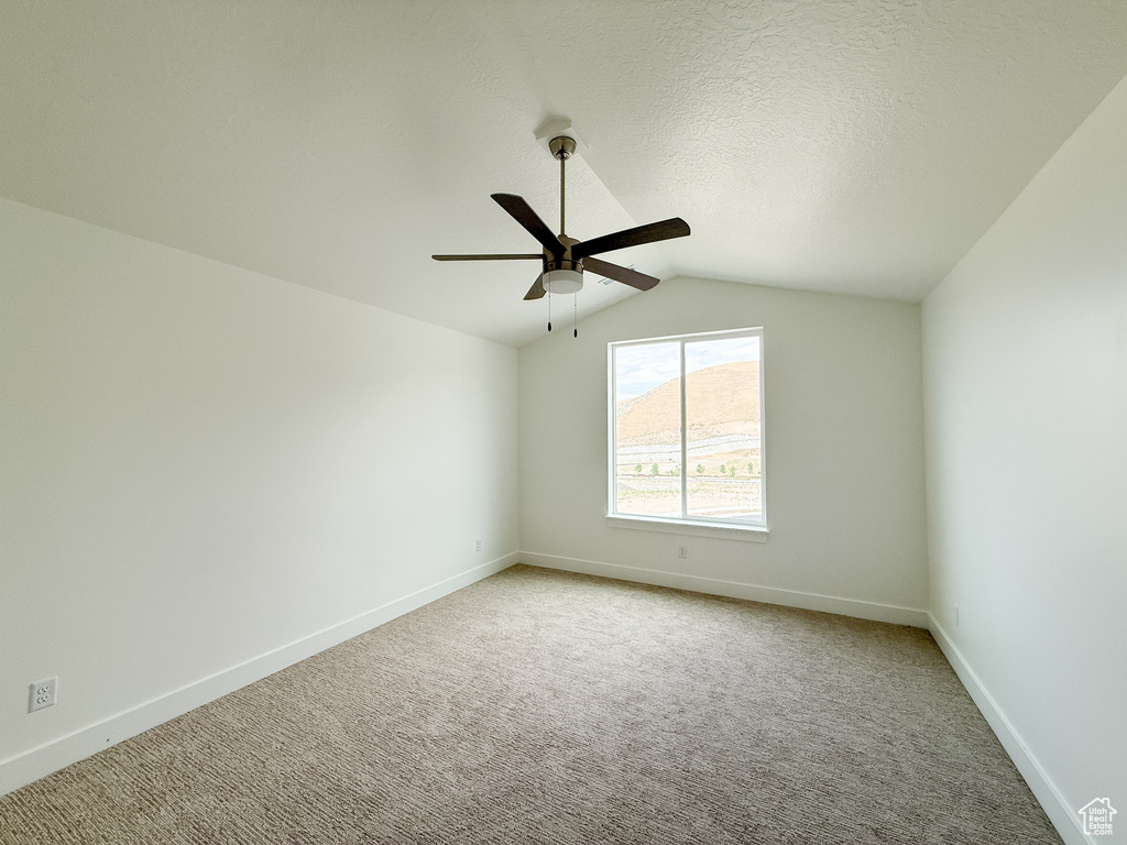 Spare room featuring lofted ceiling, ceiling fan, and light colored carpet