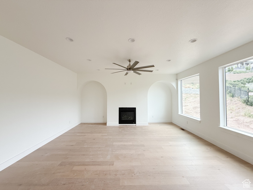 Unfurnished living room featuring light wood-type flooring, a fireplace, a ceiling fan, recessed lighting, and arched walkways