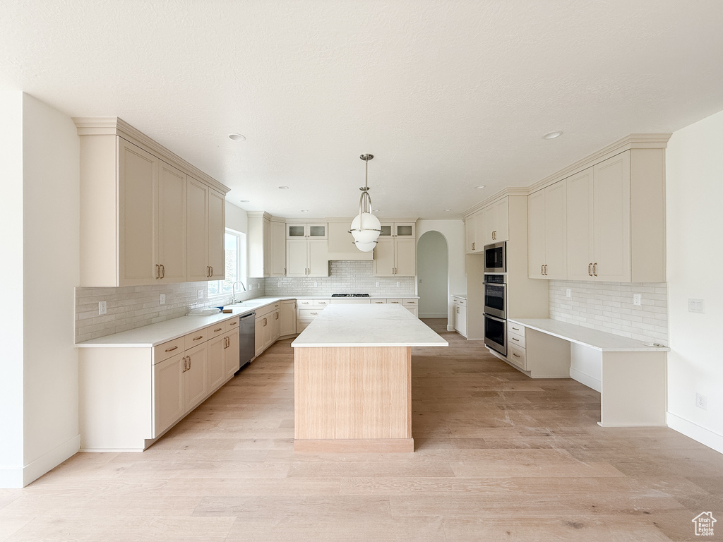 Kitchen with backsplash, a kitchen island, arched walkways, stainless steel appliances, and recessed lighting