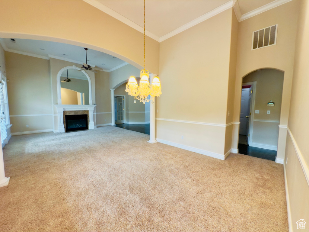 Unfurnished living room featuring a ceiling fan, carpet, ornamental molding, a fireplace, and arched walkways