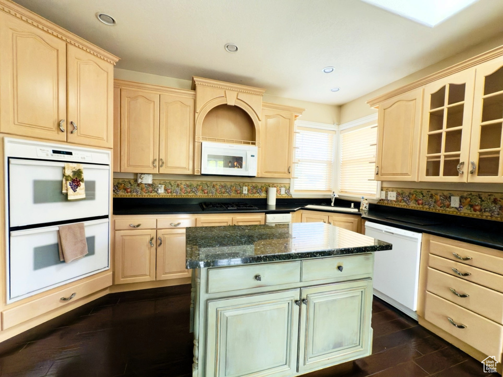 Kitchen featuring white appliances, light brown cabinets, dark wood-style flooring, a center island, and glass insert cabinets