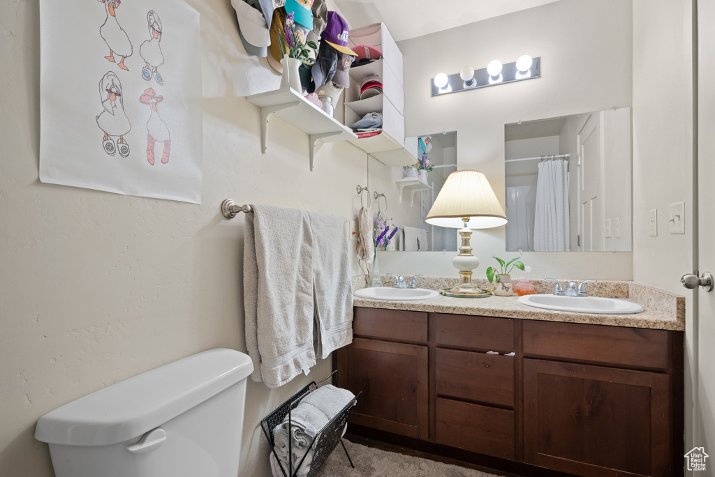 Bathroom with double vanity, a sink, curtained shower, and toilet