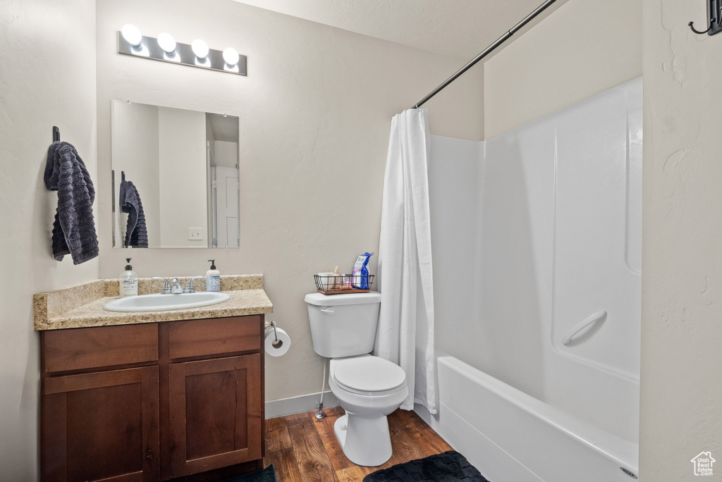 Bathroom with toilet, vanity, shower / bath combo, and wood finished floors