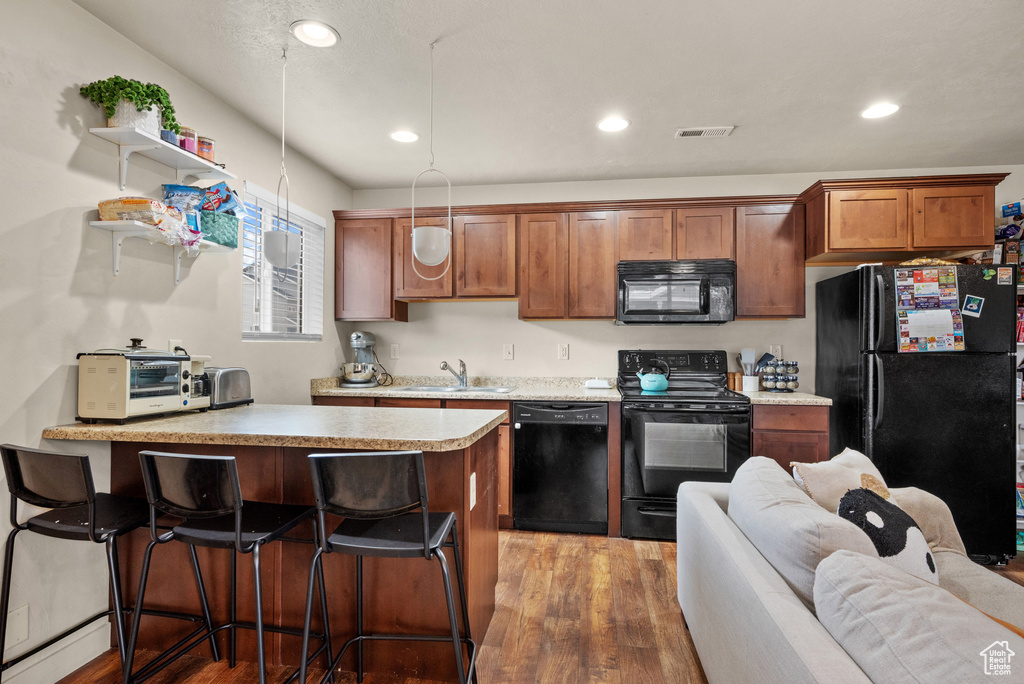 Kitchen featuring a sink, light wood finished floors, a breakfast bar area, visible vents, and black appliances