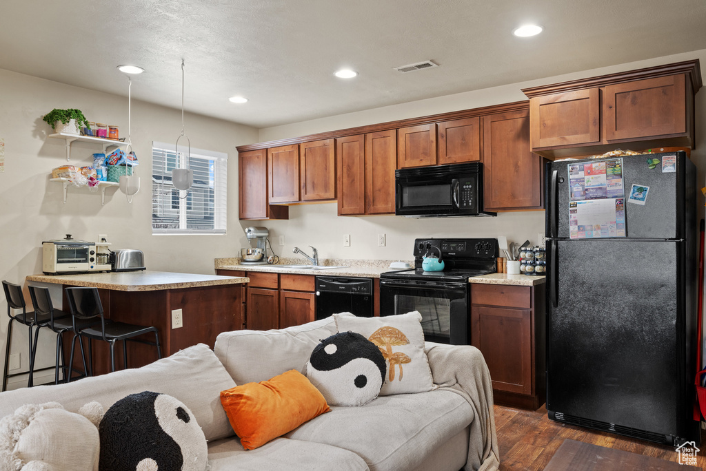 Kitchen with light countertops, a sink, dark wood-style floors, visible vents, and black appliances