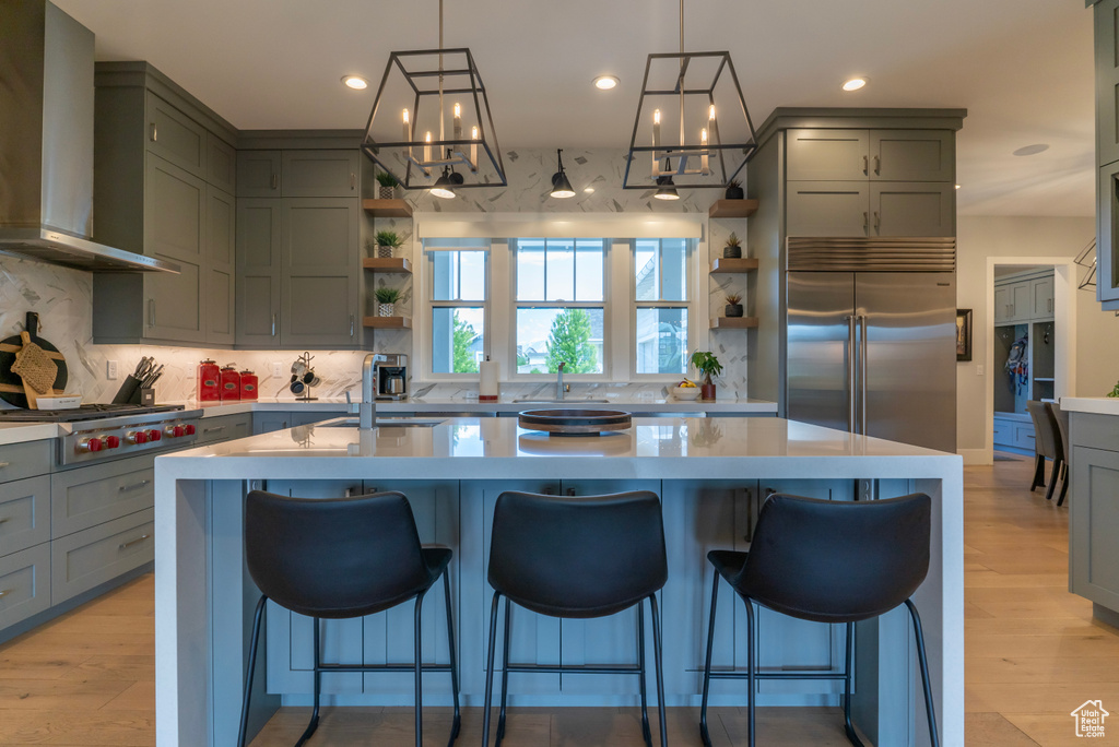 Kitchen featuring stainless steel appliances, a kitchen island with sink, light hardwood / wood-style flooring, and wall chimney exhaust hood