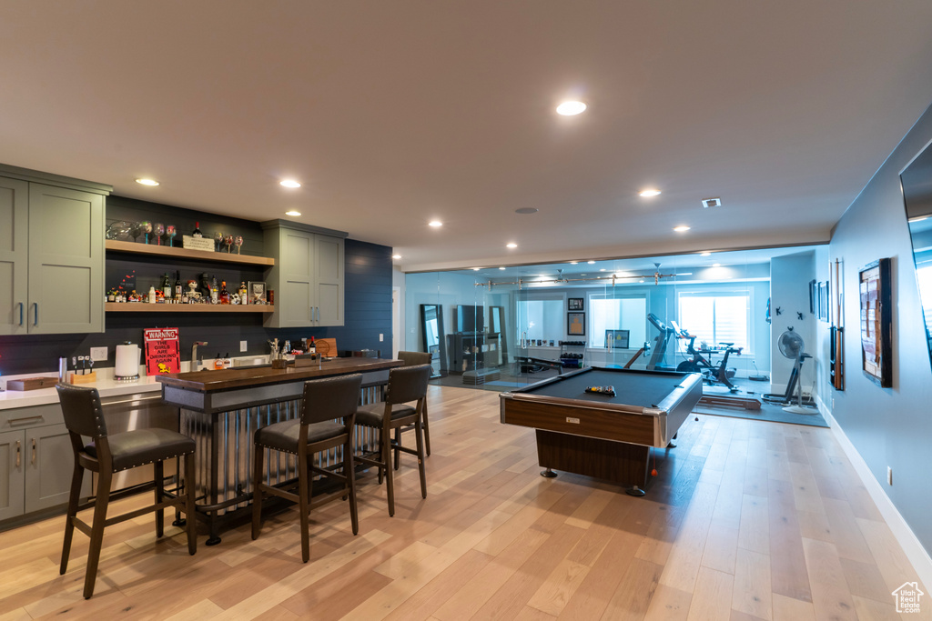 Game room with indoor bar, pool table, and light hardwood / wood-style flooring