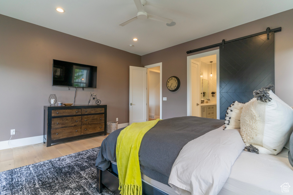 Bedroom with ceiling fan, connected bathroom, a barn door, and light wood-type flooring