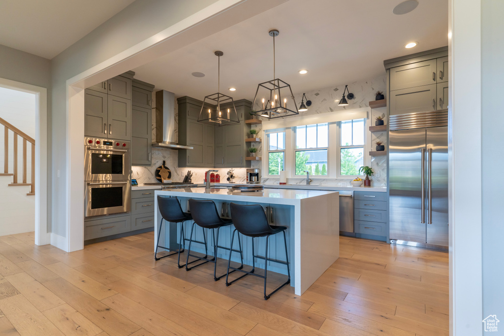 Kitchen with wall chimney exhaust hood, a kitchen bar, a kitchen island, pendant lighting, and stainless steel appliances