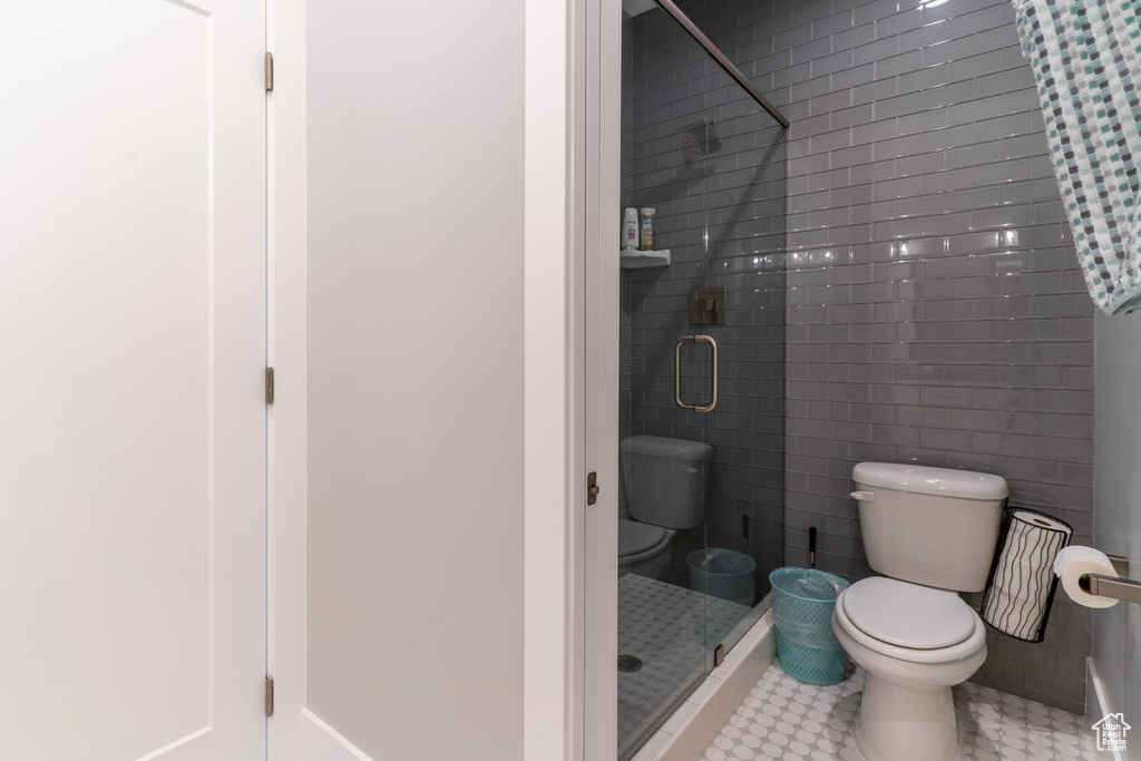 Bathroom with tile walls, a shower with shower door, tile patterned floors, and toilet