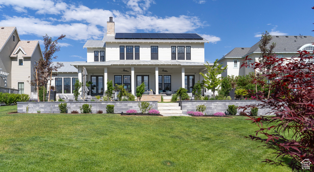 View of front of house featuring ceiling fan, a front yard, covered porch, and solar panels