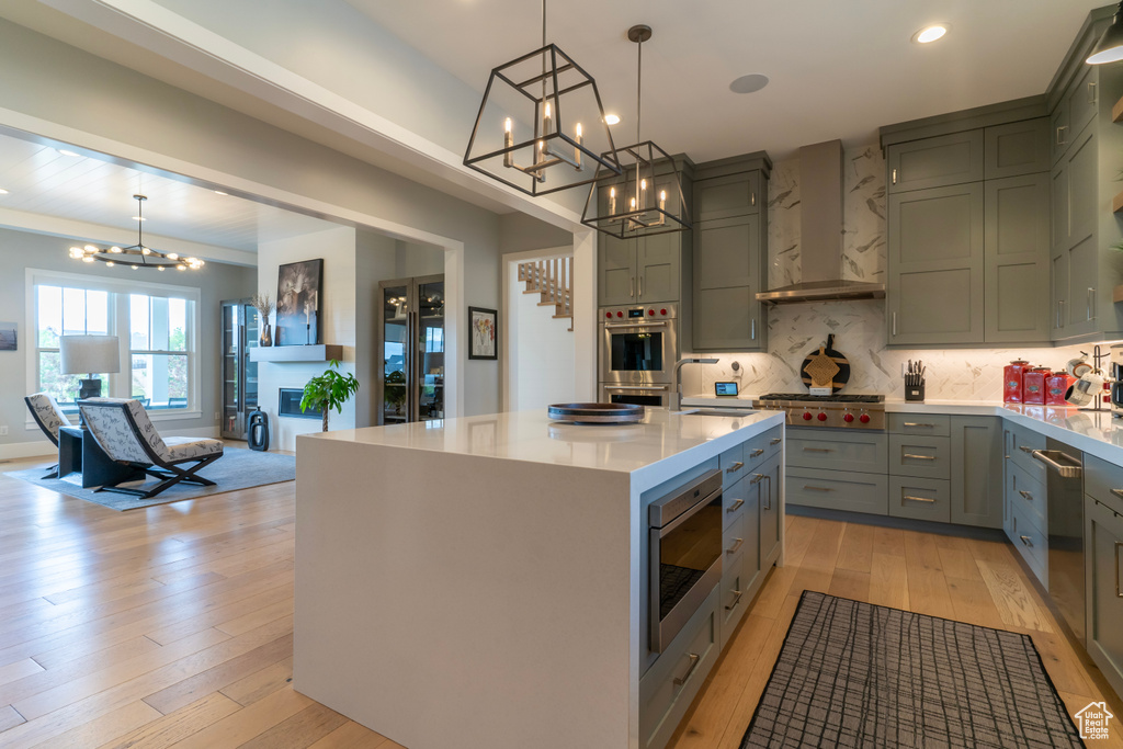 Kitchen featuring a center island, light wood-type flooring, appliances with stainless steel finishes, pendant lighting, and wall chimney range hood