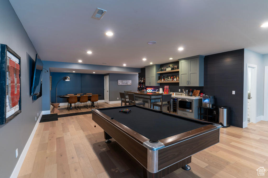 Game room with indoor bar and light hardwood / wood-style flooring