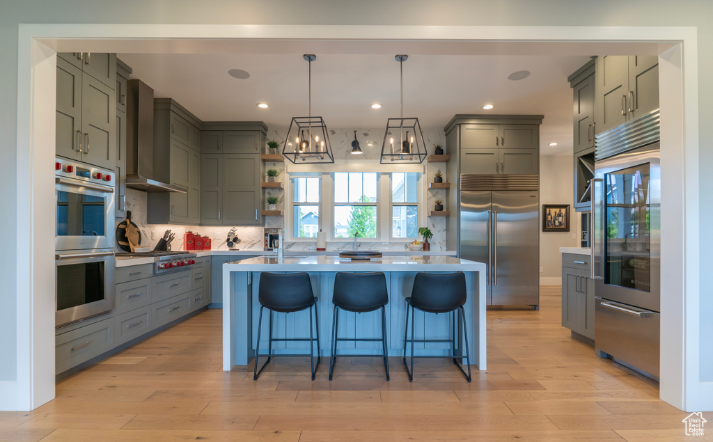 Kitchen with wall chimney exhaust hood, stainless steel appliances, a center island, and pendant lighting