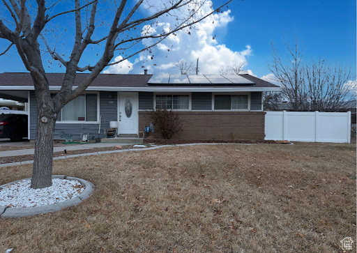 Ranch-style house featuring a front lawn and solar panels