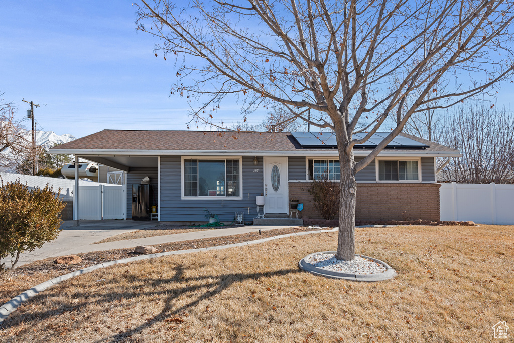 Single story home with a carport, brick siding, fence, and roof mounted solar panels