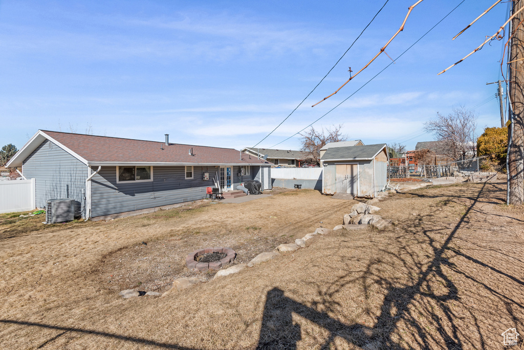 Rear view of house featuring an outbuilding, an outdoor fire pit, a fenced backyard, cooling unit, and a storage unit