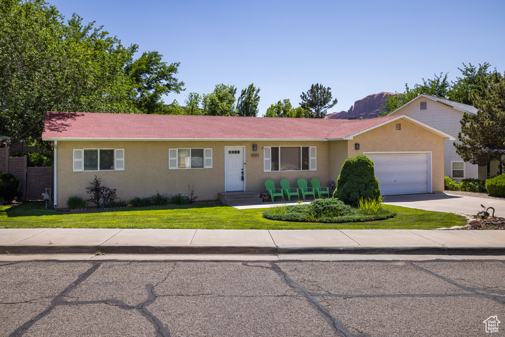 Ranch-style home with a garage, concrete driveway, stucco siding, and a front lawn