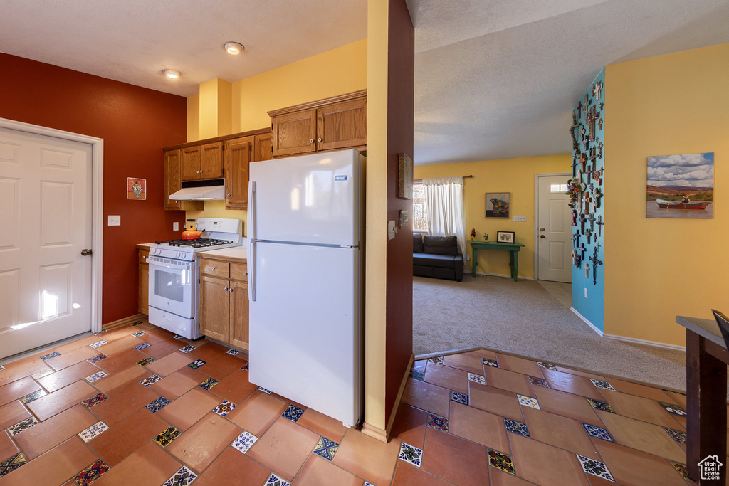 Kitchen with white appliances, under cabinet range hood, brown cabinets, light carpet, and light countertops