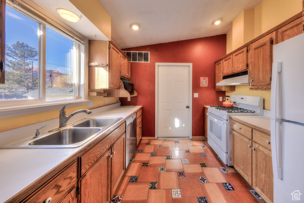 Kitchen featuring white appliances, under cabinet range hood, a sink, baseboards, and vaulted ceiling