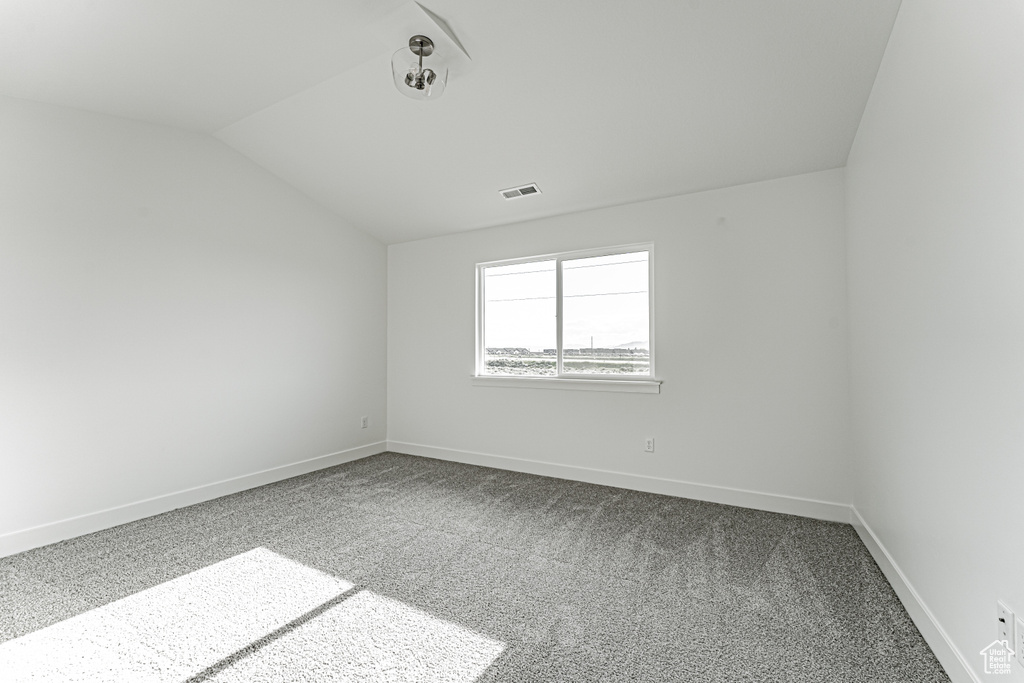 Carpeted spare room with vaulted ceiling and baseboards