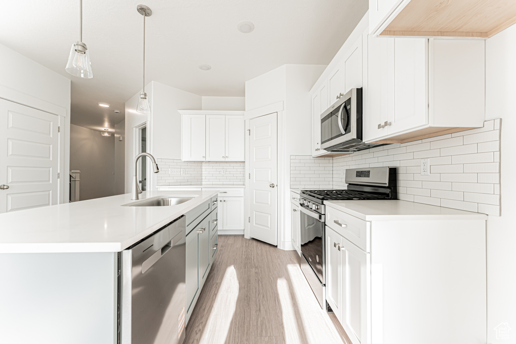 Kitchen with stainless steel appliances, a sink, light wood-style flooring, and light countertops
