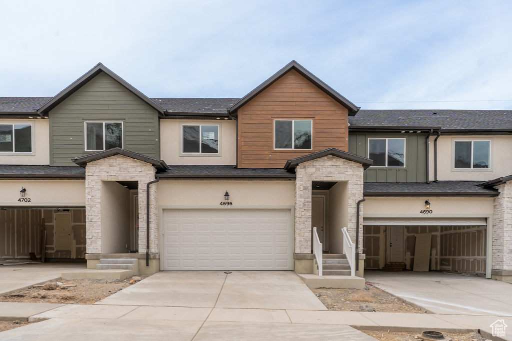 Townhome / multi-family property featuring concrete driveway, stone siding, an attached garage, and stucco siding