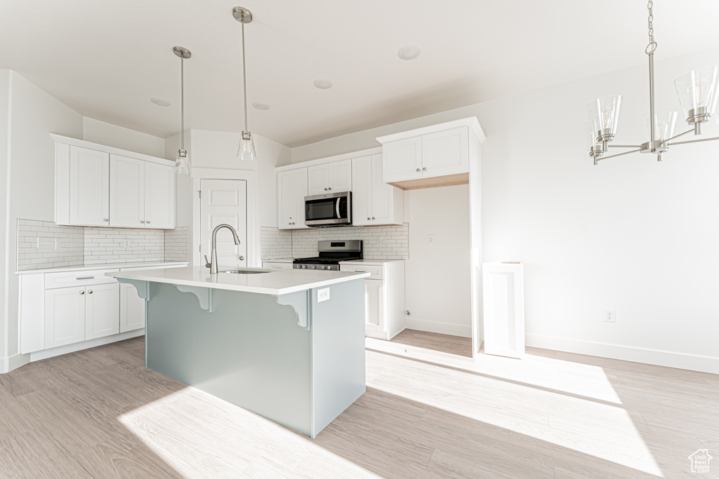 Kitchen with stainless steel appliances, a sink, light wood finished floors, light countertops, and backsplash
