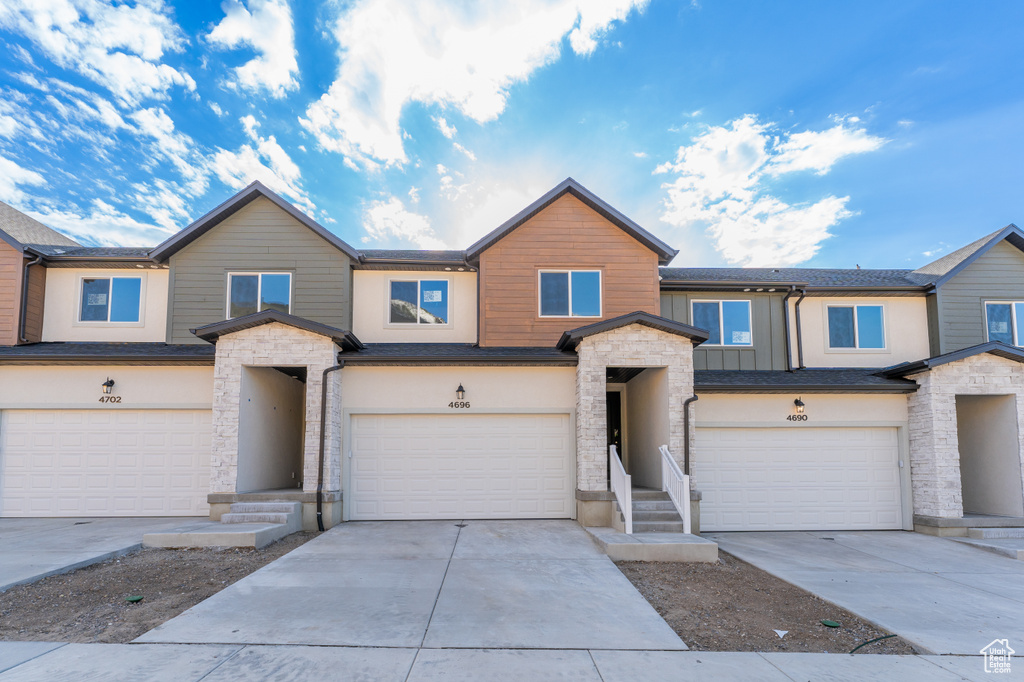 View of property featuring a garage, stone siding, concrete driveway, and stucco siding