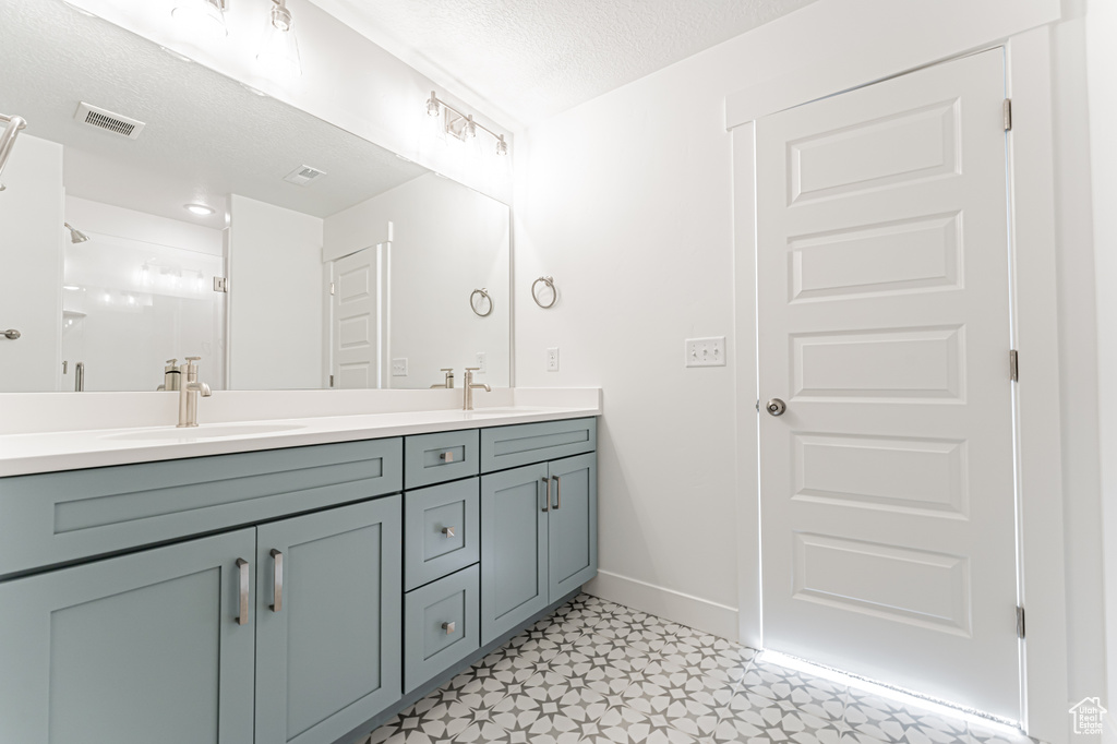 Bathroom featuring double vanity, tile patterned floors, baseboards, a textured ceiling, and a shower