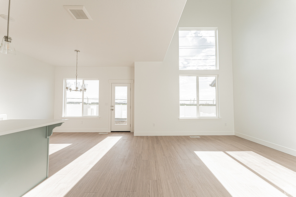 Unfurnished living room featuring a chandelier, light wood-type flooring, and baseboards