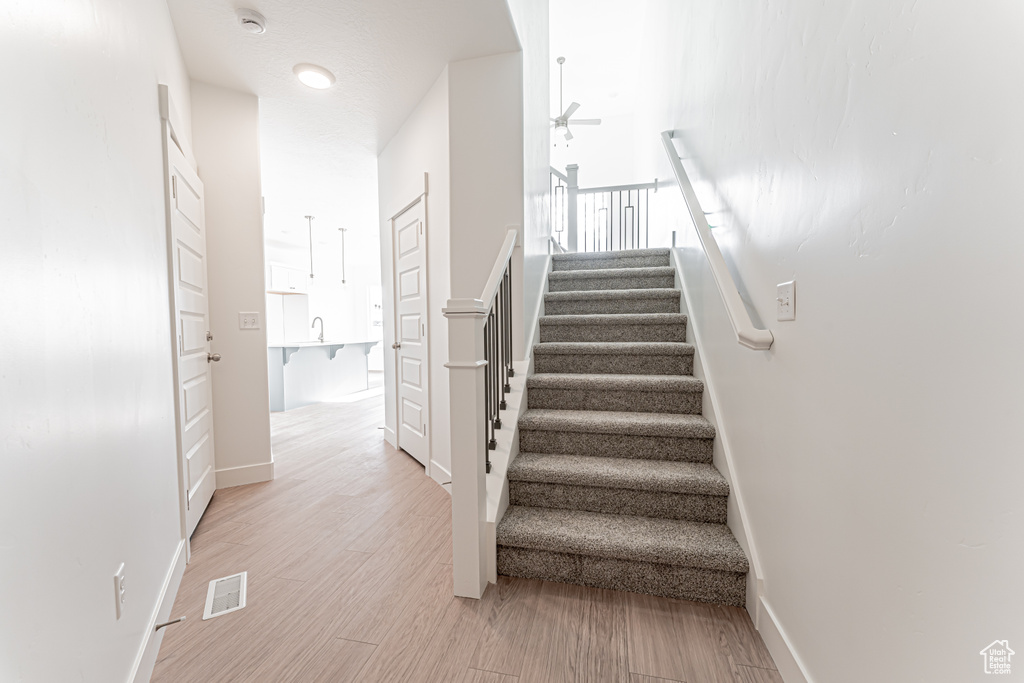 Stairway with ceiling fan, baseboards, and wood finished floors
