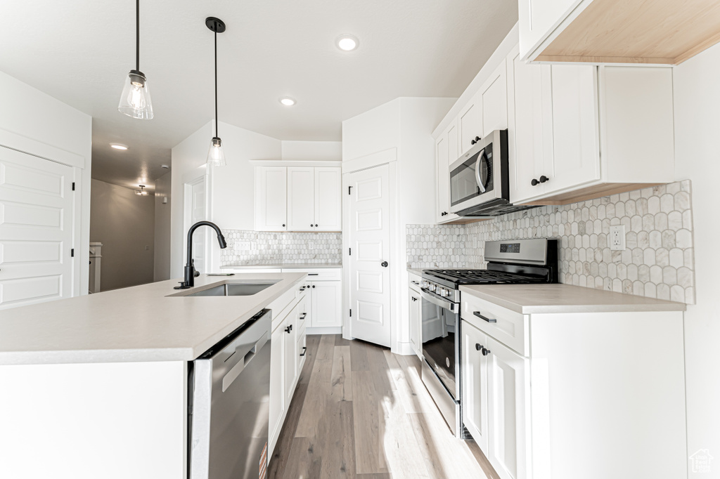 Kitchen with stainless steel appliances, a sink, a center island with sink, light countertops, and recessed lighting